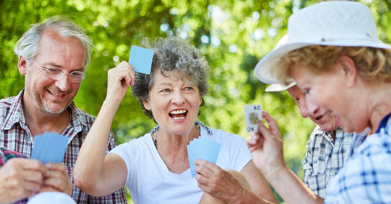 Eine Gruppe Senioren sitzt im Grünen und spielt Karten