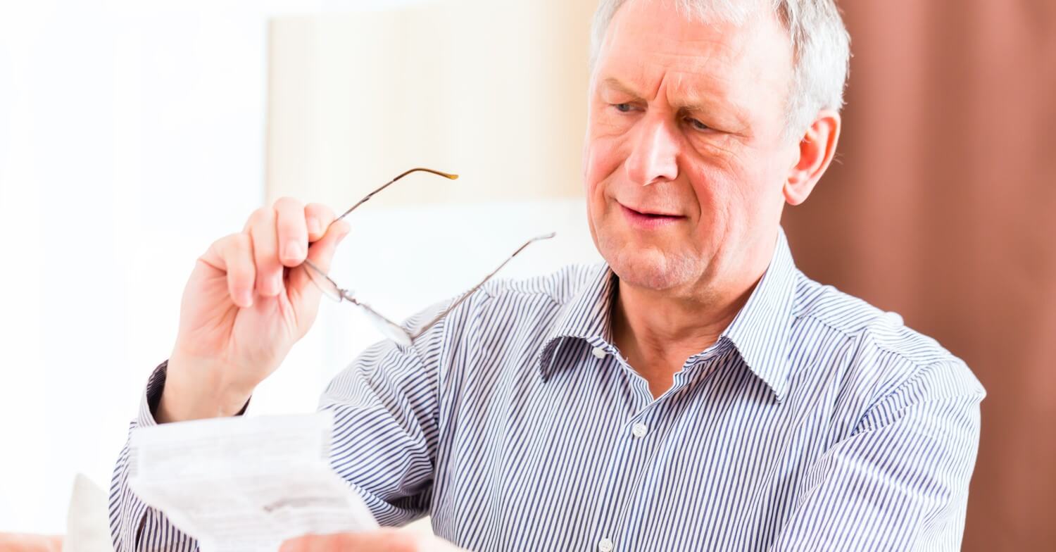 Ein älterer Mann versucht einen Beipackzettel zu lesen. Er hält ihn weit von sich entfernt und hält seine Brille in der Hand