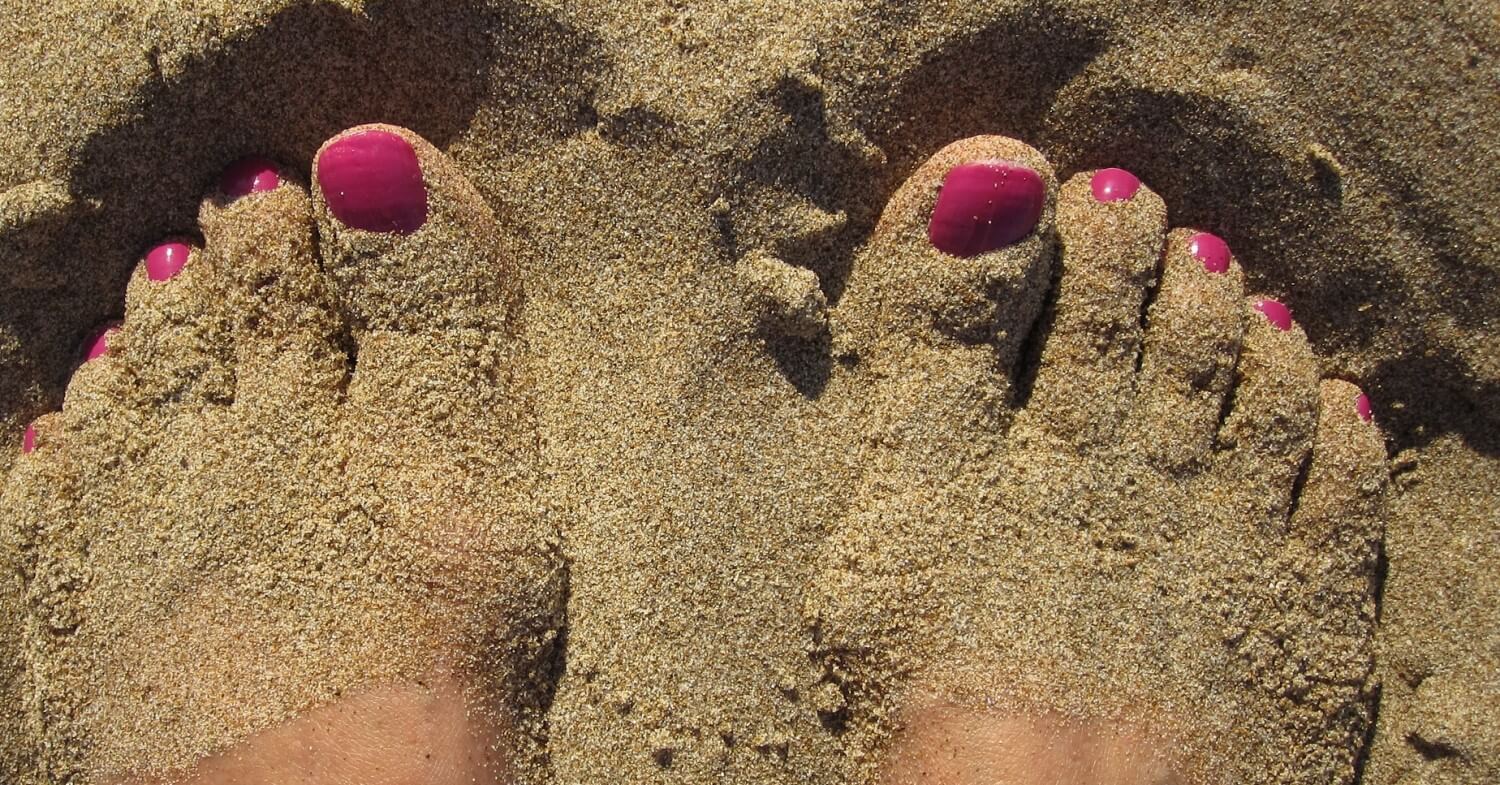 Füße mit pinkfarbig lakierten Nägeln im Sand