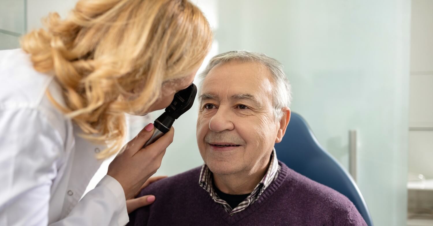 Eine Augenärztin untersucht einen Senior. Der Patient ist der Kamera zugewandt, von der Ärztin sind nur der Oberkörper und der Hinterkopf zu sehen