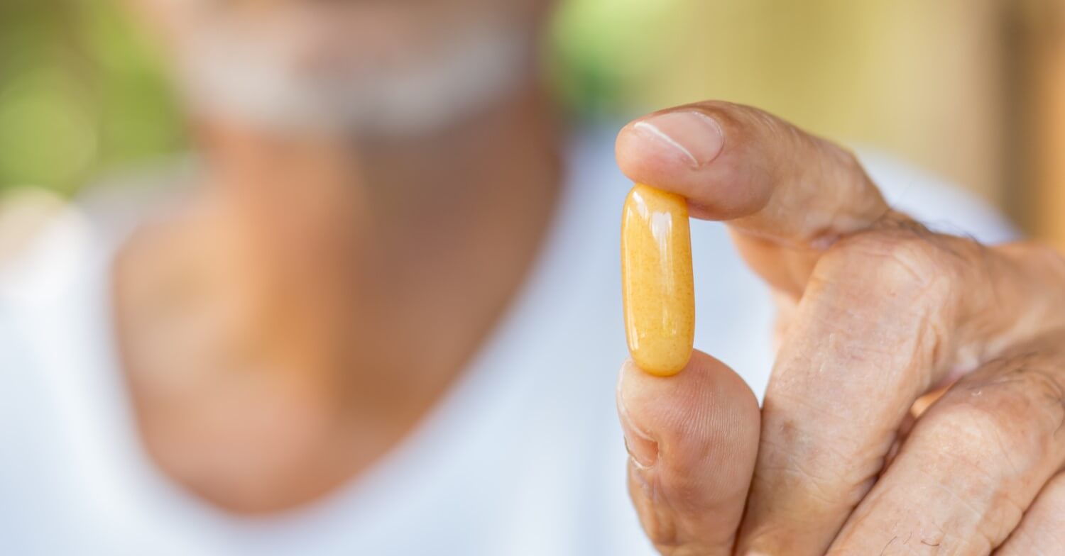 Ein älterer Mann hält eine Tablette zwischen Daumen und Zeigefinger in die Kamera