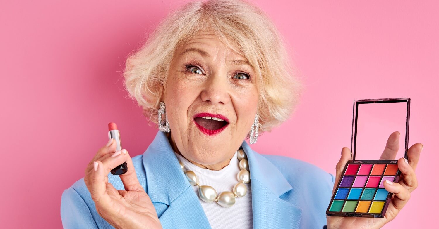 Blonde Seniorin hält einen Lippenstift und eine Palette mit Wimperntusche in der Hand