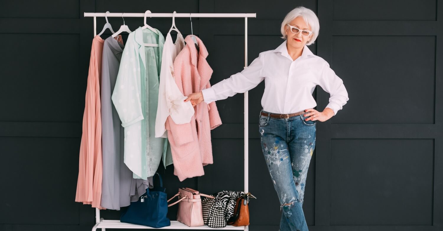 Eine Seniorin in Jeans und weißer Bluse präsentiert Handtaschen und Mode für Damen