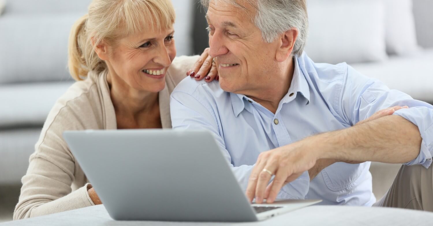 Ein Rentnerpaar sitzt lachend vor einem Notebook