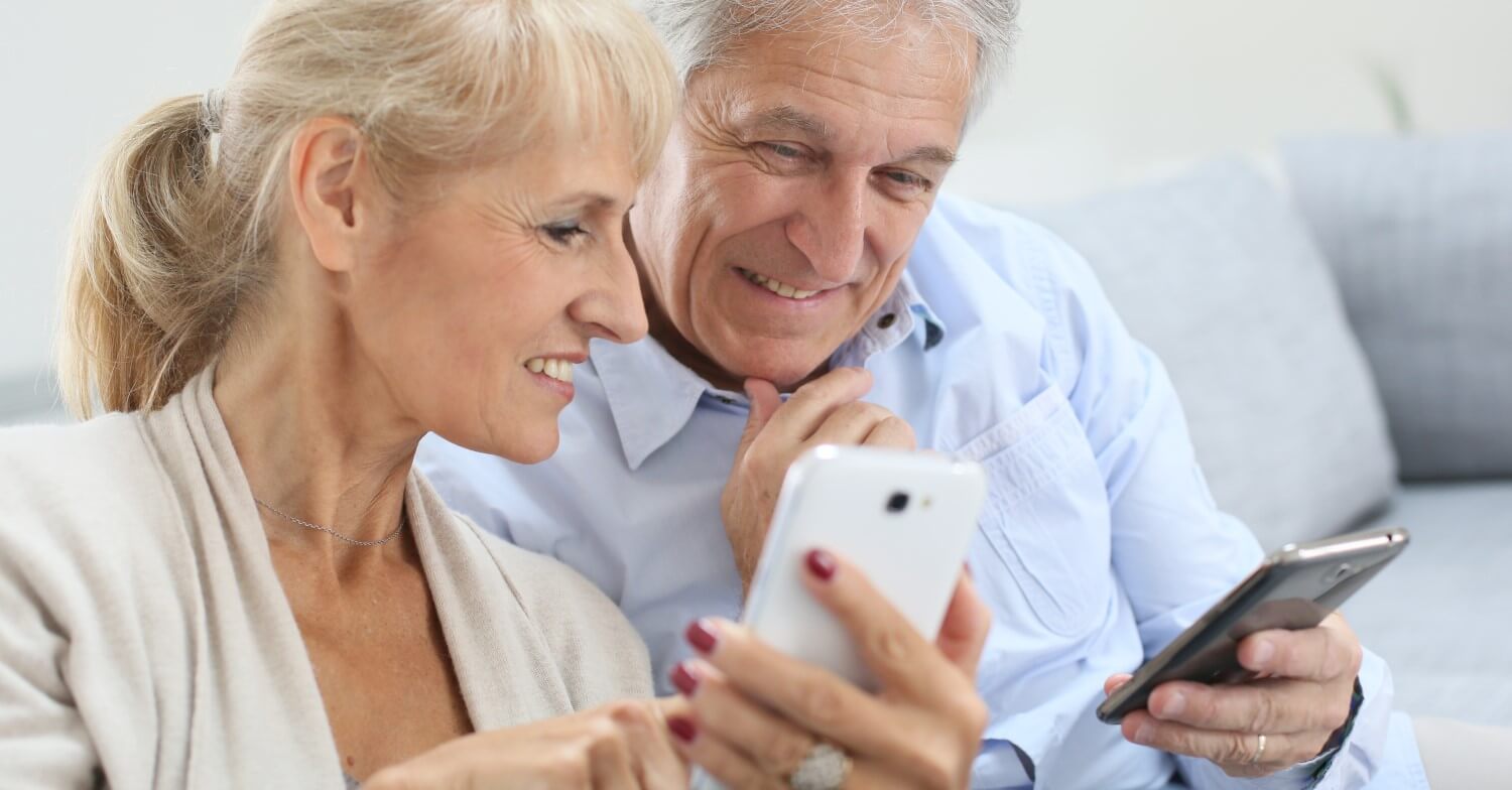 Zwei Senioren sitzen auf dem Sofa und benutzen ihre Smartphones